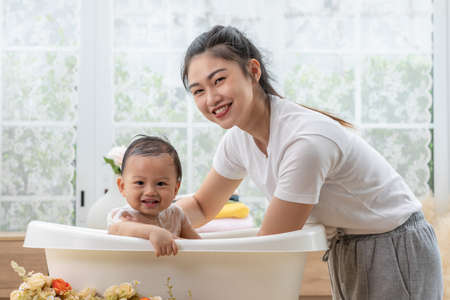 Calm asian baby bathing in bathtub enjoy laughing. mother bathing her son in warm water.Happy adorable newborn infant smile in tub relax and comfortable good moment with mom. Newborn baby care conceptの写真素材