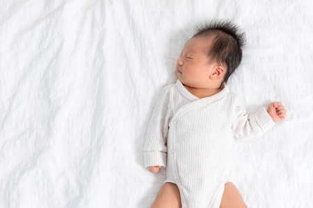 Top view happy newborn baby lying sleeps on a white blanket comfortable and safety at warmth place. Cute Asian newborn sleeping and napping on bed. Newborn Baby Care conceptの写真素材
