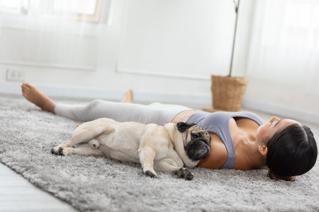 Asian woman doing yoga with her pug breed dog in a peaceful setting, cultivating a sense of harmony and wellness in both body and mind. Self Care Concept.の写真素材
