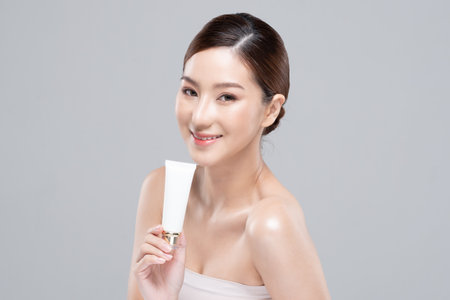 Beautiful Young Asian Woman Holding luxury white clean tube smile feeling so happy and cheerful with healthy Clean and Fresh skin,isolated on gray background,Beauty Cosmetics spa and treatment Conceptの写真素材