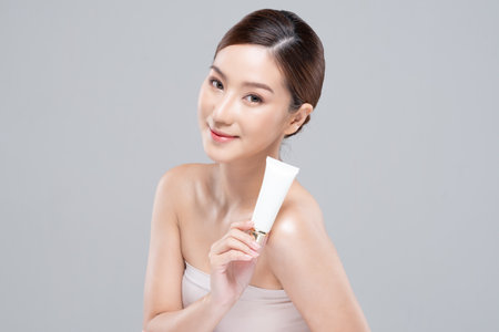 Beautiful Young Asian Woman Holding luxury white clean tube smile feeling so happy and cheerful with healthy Clean and Fresh skin,isolated on gray background,Beauty Cosmetics spa and treatment Conceptの写真素材