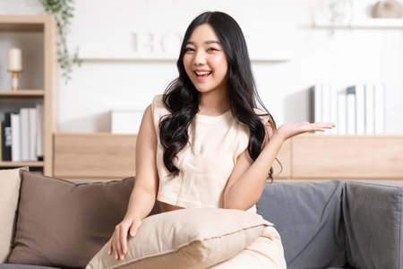 Happy attractive asian young woman smile and open hand palm to copy space at home. Cheerful pretty girl wear casual dress open palm to empty space for mockup to display productの写真素材