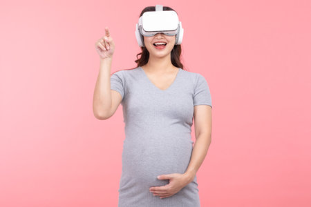 Happy Pregnant Woman using virtual reality glasses standing smile and stroking big belly with love isolated on white background.Pregnancy Metaverse Technology Conceptの写真素材
