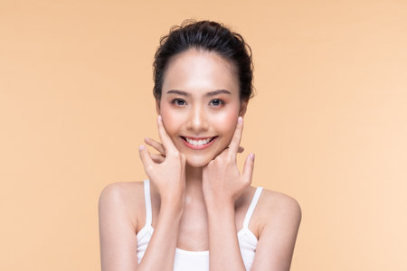 Beautiful Asian young woman touching soft cheek smile with clean fresh skin Happiness and cheerful with positive emotional,isolated on Beige background,Beauty Cosmetics and Facial treatment Conceptの写真素材