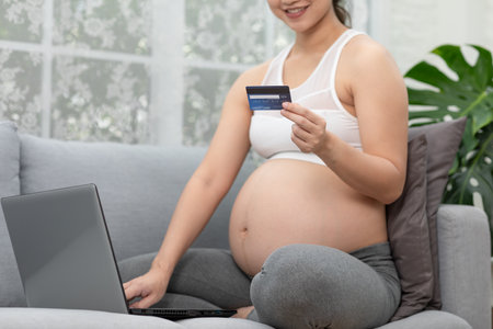 Happy pregnant woman using credit card shopping online at home.Mother purchasing baby clothes from internet online store by Computer laptop.Pregnancy Shopping Online Conceptの写真素材