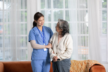 Happy asian female doctor helping elderly patient walking with cane or walking stick at home.Nures...