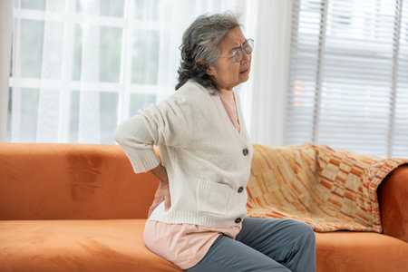 Asian Elderly senior woman back pain and illness on sofa alone at home,unhappy elderly touch on back serious and tried,Elderly Care and insurance Conceptの写真素材