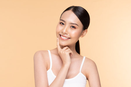 A young woman smiling and posing thoughtfully against a warm, soft background, showcasing confidence and joy.の写真素材