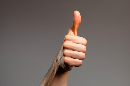 Close-up of human hand showing thumbs up sign on grey backgroundの素材