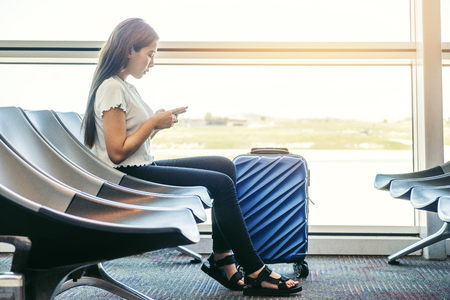 Asian Traveler women looking for flight in smartphone at airport terminal Travel conceptの写真素材