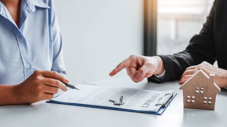 Sale Agent giving house keys to woman customer and sign agreement documents for realty purchase.の写真素材
