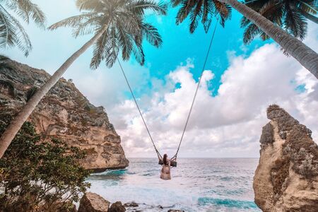 Beautiful girl on swing coconut palms on beach at Diamond  beach, Nusa Penida island Bali, Indonesiaの写真素材