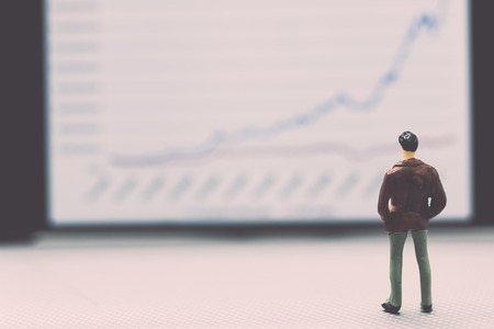 Miniature people : small figures businessmen stand and look at the graph on the phone display with copy space and using as background finance business team competition concept.の写真素材