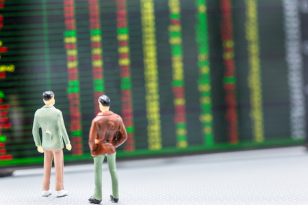 Miniature people : small figures businessmen stand and look at Stock Exchange Board Background with copy space and using as background finance business team competition concept, business plan concept.の写真素材
