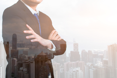 Double exposure of Cropped portrait young businessman with his cross one arm. City and bay on the Blurred background with light. horizontal, using as Business Concept, business success concept.の写真素材