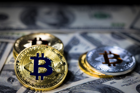 Pile of stacking Golden bitcoin on one hundred dollar banknotes. single coin facing the camera in sharp focus with shading on the icon letter B on the face of the bitcoin, Business and trading concept.の写真素材