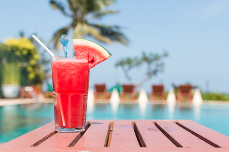 Healthy concept, Water melon smoothie on a wood table with swimming pool and blue sky background.の写真素材