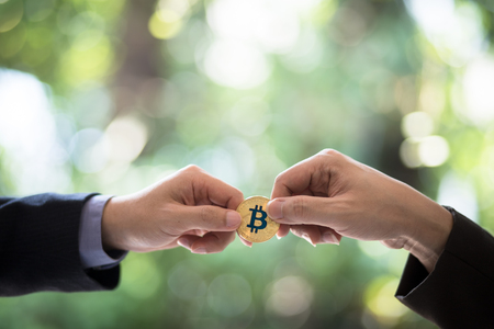 Hands of two businessmen are trading coin of bitcoin. A symbolic coins of bitcoin. electronic money exchange, Business, Digital currency, Finance and technology concept. Garden bokeh background.の写真素材