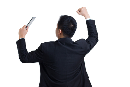 Modern asian businessman wear black suit stand up to the back and holding digital tablet celebrating successful. Businessman happy and smile with Arms up while standing isolated on white background.の写真素材