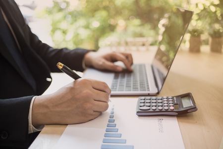 Close up shot of a businessman writing on charts paper at workstation. Modern business man writing on chart paper and using laptop computer. Business concept, Marketing plan, Successful Business.の写真素材