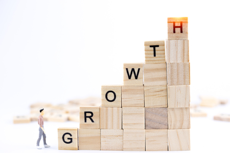 Miniature people small figure walking on wooden cube with word GROWTH isolated on white background. With copy space for your text. Business success, business growth, leadership concept.の写真素材
