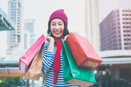 Portrait of an excited beautiful young girl wear shirt and wool hat holding many shopping bags and smile. With copy space. Woman shopper smiling happy. Beautiful young Caucasian. lifestyle, discountの写真素材