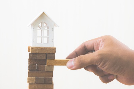 Hand holding wood block with model white house on wood block game. Investment risk and uncertainty in the real estate housing market. Property investment and house mortgage financial concept. Copy space.の写真素材