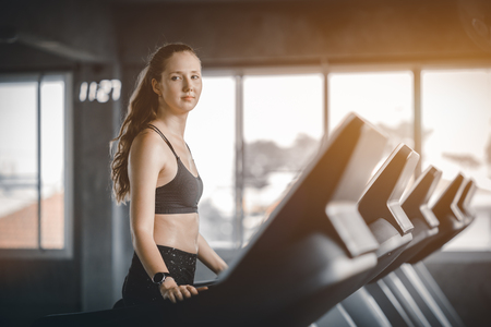 Fit young woman caucasian running on machine treadmill workout in gym. Glad smiling girl is enjoy with her training process. Concept of fitness, healthy life, Sport, Lifestyle.の写真素材