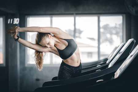 Young woman attractive fitness exercise workout in gym. Woman stretching the muscles and relaxing after exercise on machine treadmill at fitness gym club.の写真素材