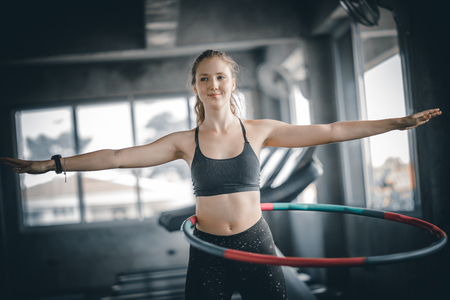 Beautiful caucasian young woman doing hula hoop in step waist hooping forward stance. Young woman doing hula hoop during an exercise class in a gym. Healthy sports lifestyle, Fitness, Healthy concept.の写真素材