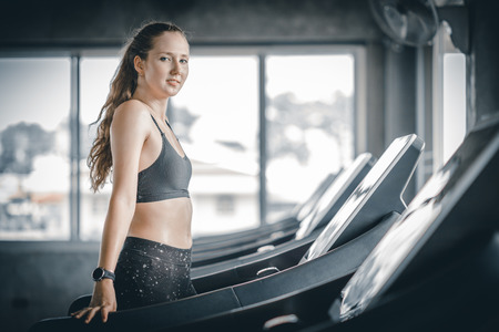 Fit young woman caucasian running on machine treadmill workout in gym. Glad smiling girl is enjoy with her training process. Concept of fitness, healthy life, Sport, Lifestyle.の写真素材