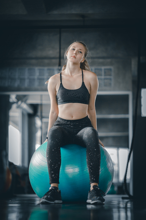 Young attractive woman fitness doing exercises workout on ball in gym. Woman stretching the muscles and relaxing after exercise at fitness gym club.の写真素材