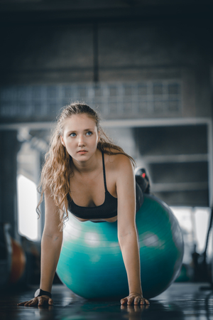Young attractive woman fitness doing hard difficult plank on ball in gym workout. Woman stretching the muscles and relaxing after exercise at fitness gym club.の写真素材