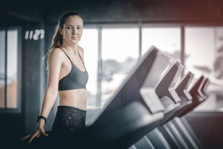Fit young woman caucasian running on machine treadmill workout in gym. Glad smiling girl is enjoy with her training process. Concept of fitness, healthy life, Sport, Lifestyle.の写真素材