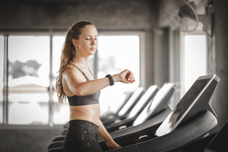 Fit young woman caucasian running on machine treadmill workout in gym. Glad smiling girl is enjoy with her training process. Concept of fitness, healthy life, Sport, Lifestyle.の写真素材