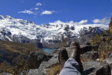 Scene of the shoes of a tourist who is resting on the Andean peaks and in the background is the snowy Huaytapallanaの写真素材