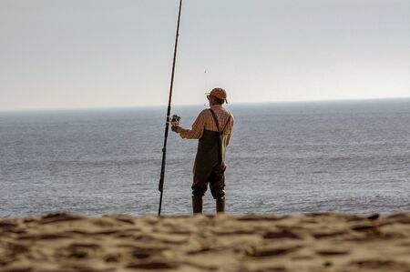 Fisherman on beach shore with fishing rodの写真素材