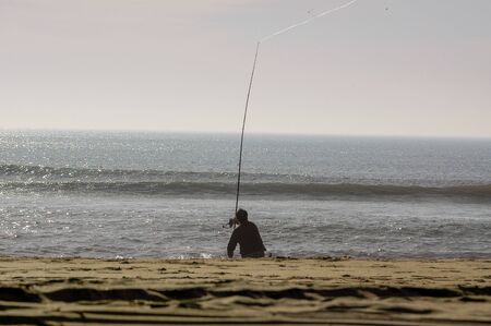 Fisherman on beach shore with fishing rodの写真素材