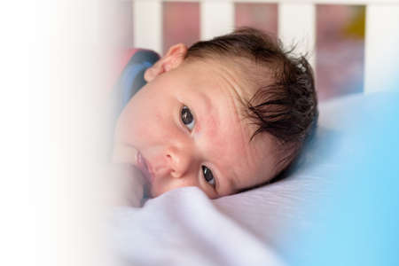 Cute little baby lying in baby crib with red cape and blue short-sleeved shirtの写真素材