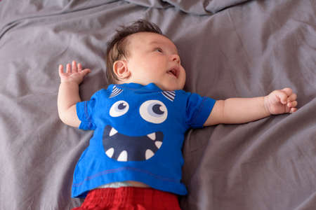 Cute little baby lying in baby crib with red cape and blue short-sleeved shirtの写真素材