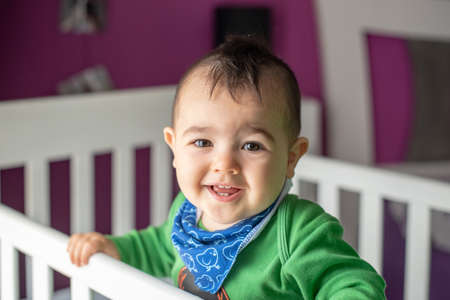 Cute little punk style baby with green t-shirt and blue scarf in white crib