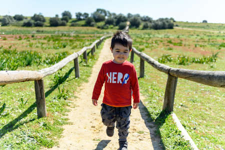 Little boy in red shirt on green meadow with dirt footpathの写真素材
