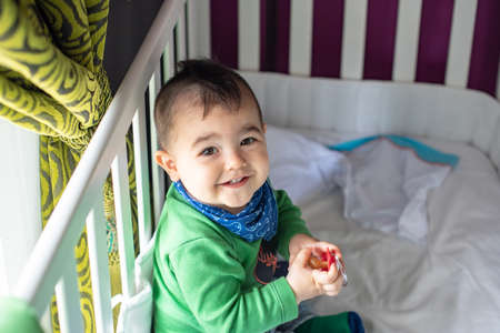 Cute little punk style baby with green t-shirt and blue scarf in white crib
