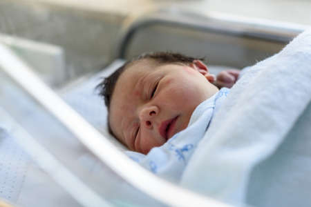 Newborn baby with days of life lying in hospital crib in maternity ward