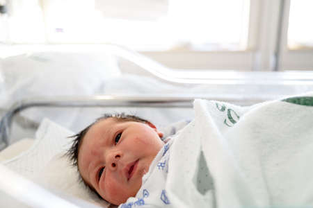 Newborn baby with days of life lying in hospital crib in maternity ward
