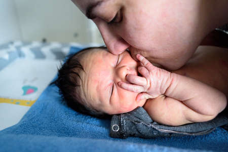 Mother kissing newborn lying baby on faceの写真素材