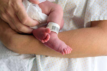 Newborn feet in hospital with diaper, baby gown and identification bracelet on the foot