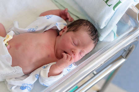 Newborn baby lying in hospital bed with baby gown