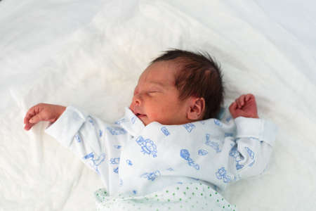 Newborn baby lying in hospital bed with baby gown
