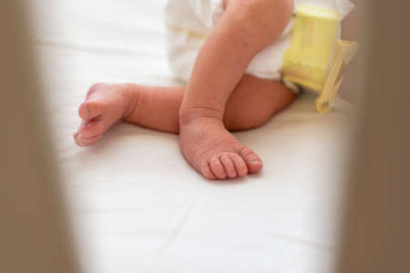 Feet of newborn baby with diaper lying asleep in home crib.